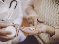 An older woman with a handful of oral medications.